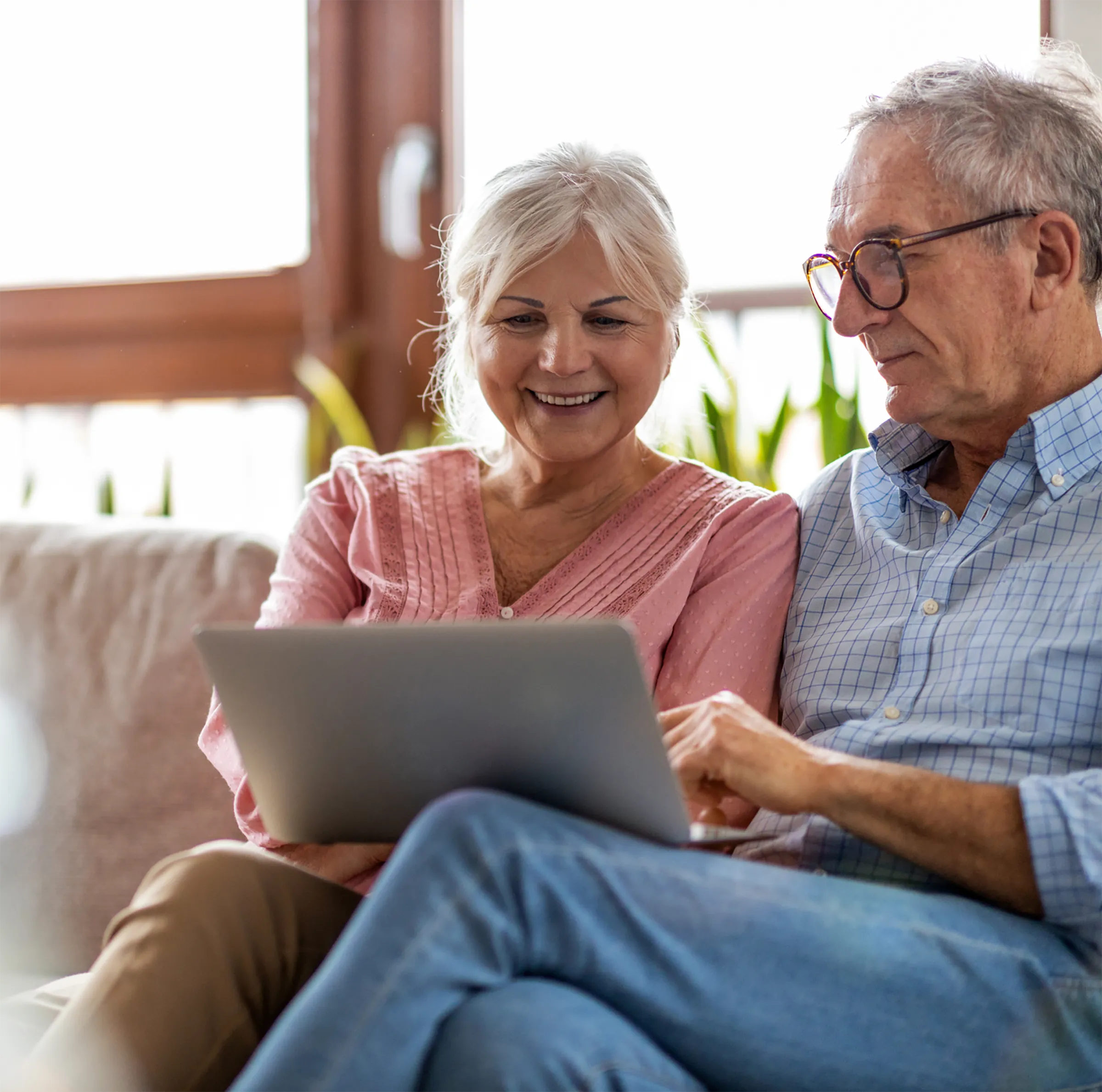 An old couple sitting together on a couch looking at a laptop